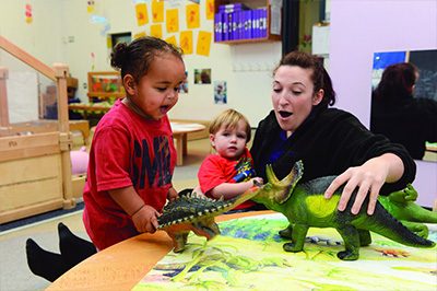 A woman and two children happily playing with toys in a classroom