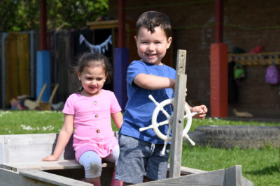 Close up of 2 children playing on an outdoor wooden pirate ship